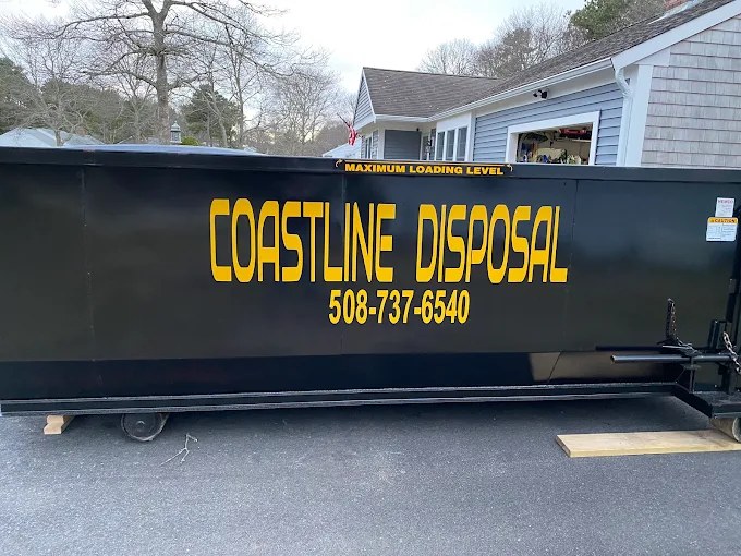 Black Coastline Disposal roll-off dumpster with gold lettering on a Cape Cod driveway